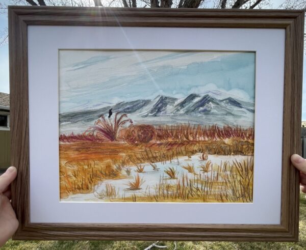 Watercolor painting of a desert mountain scape featuring blue snowy moutons in the background, orange and yellow grassy middle ground and a marshy reflective foreground.